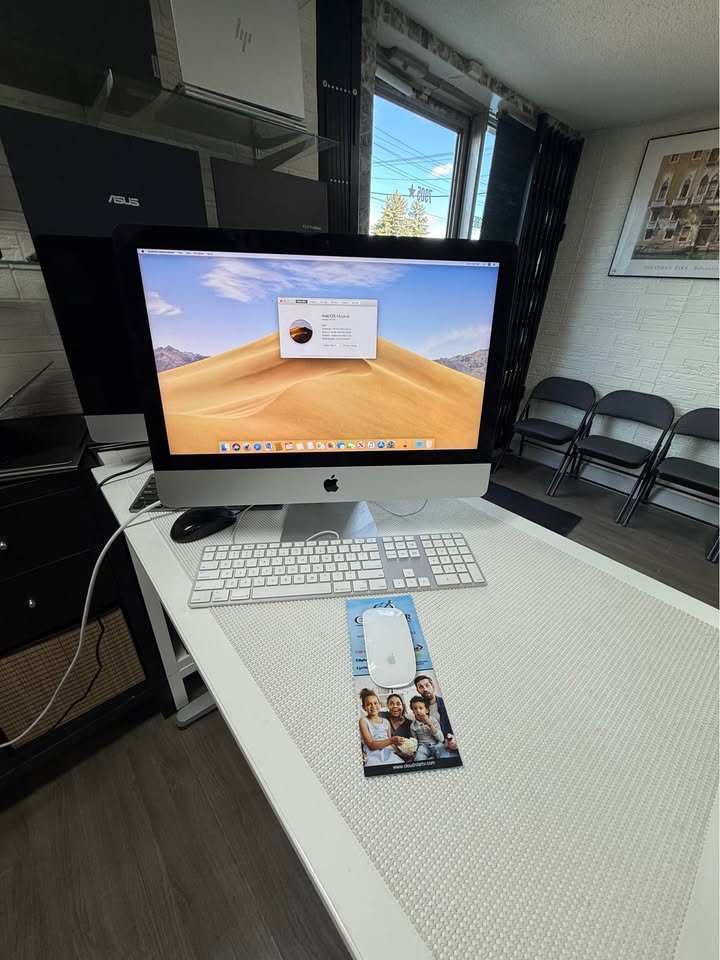 Apple iMac 21.5-inch on a desk with Apple keyboard and mouse, showing macOS About This Mac