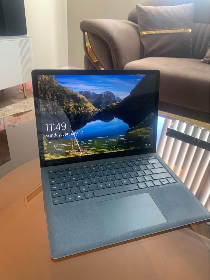 Microsoft Surface Laptop 3 open on a glass table showing the lock screen